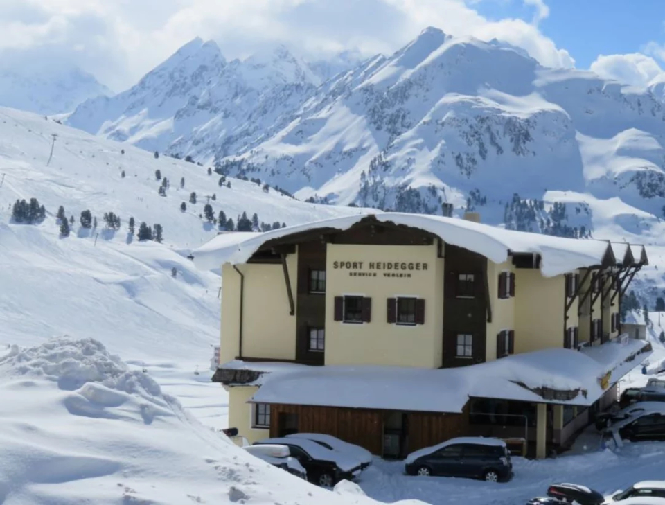 INTERSPORT Heidegger Hauptgeschäft von außen mit gelber Fassade, im Hintergrund ist die Skipiste zu sehen.