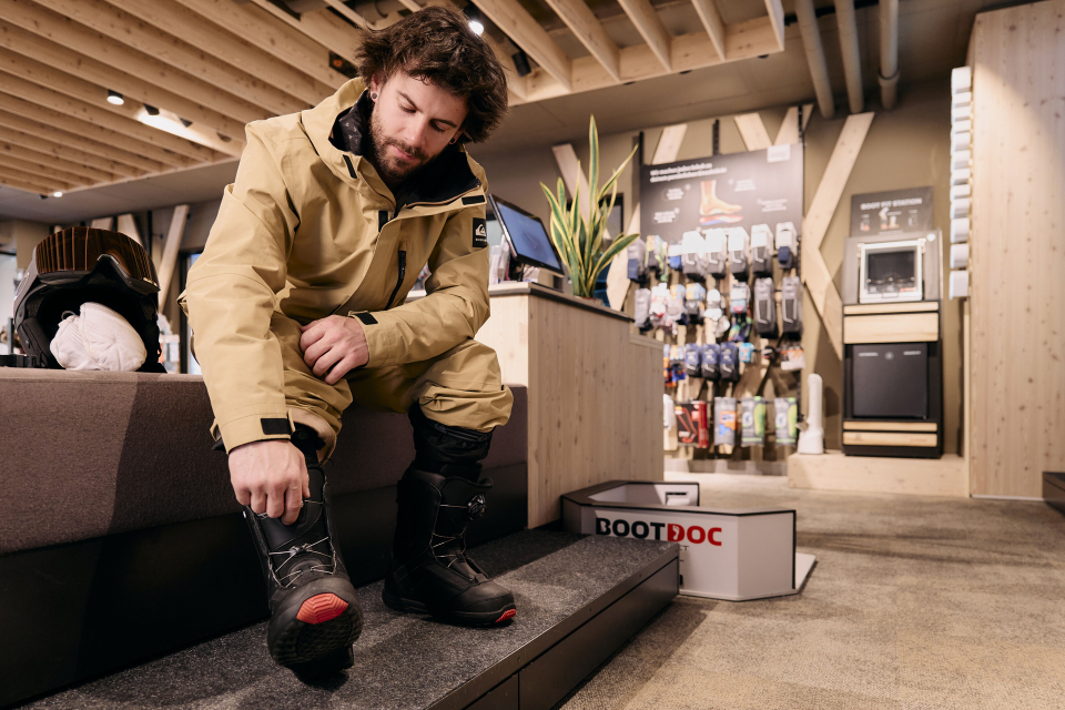 Ein Mann sitzt auf einer Bank im Laden und zieht Skischuhe an.