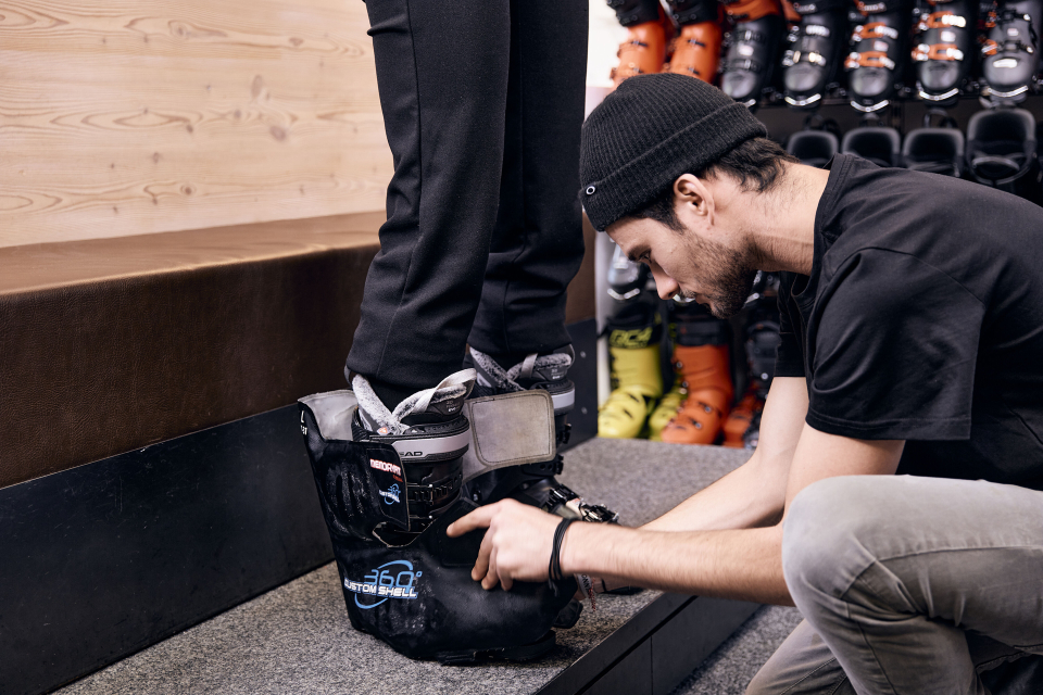 Mitarbeiter sieht sich die Skischuhe eines Kunden an