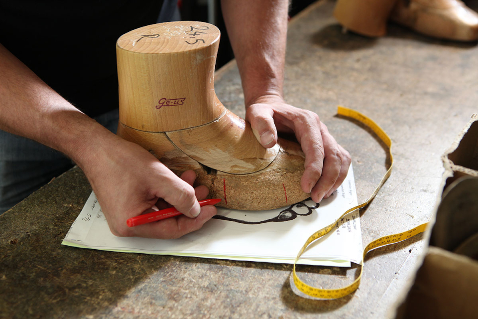 Mitarbeiter zeichnet von einer Holzvorlage die Fußform auf Papier
