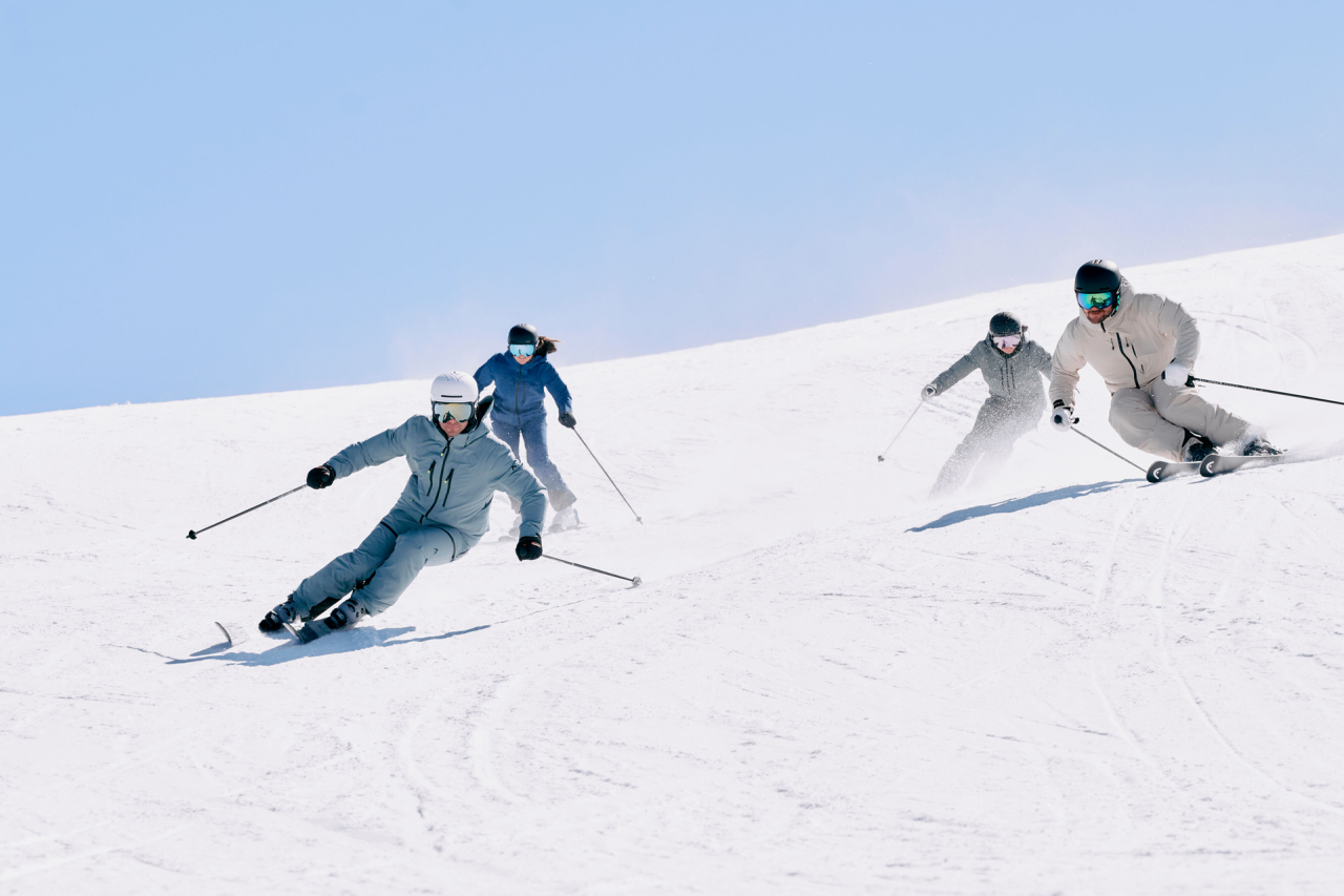 4 Skifahrer fahren die Piste hinunter