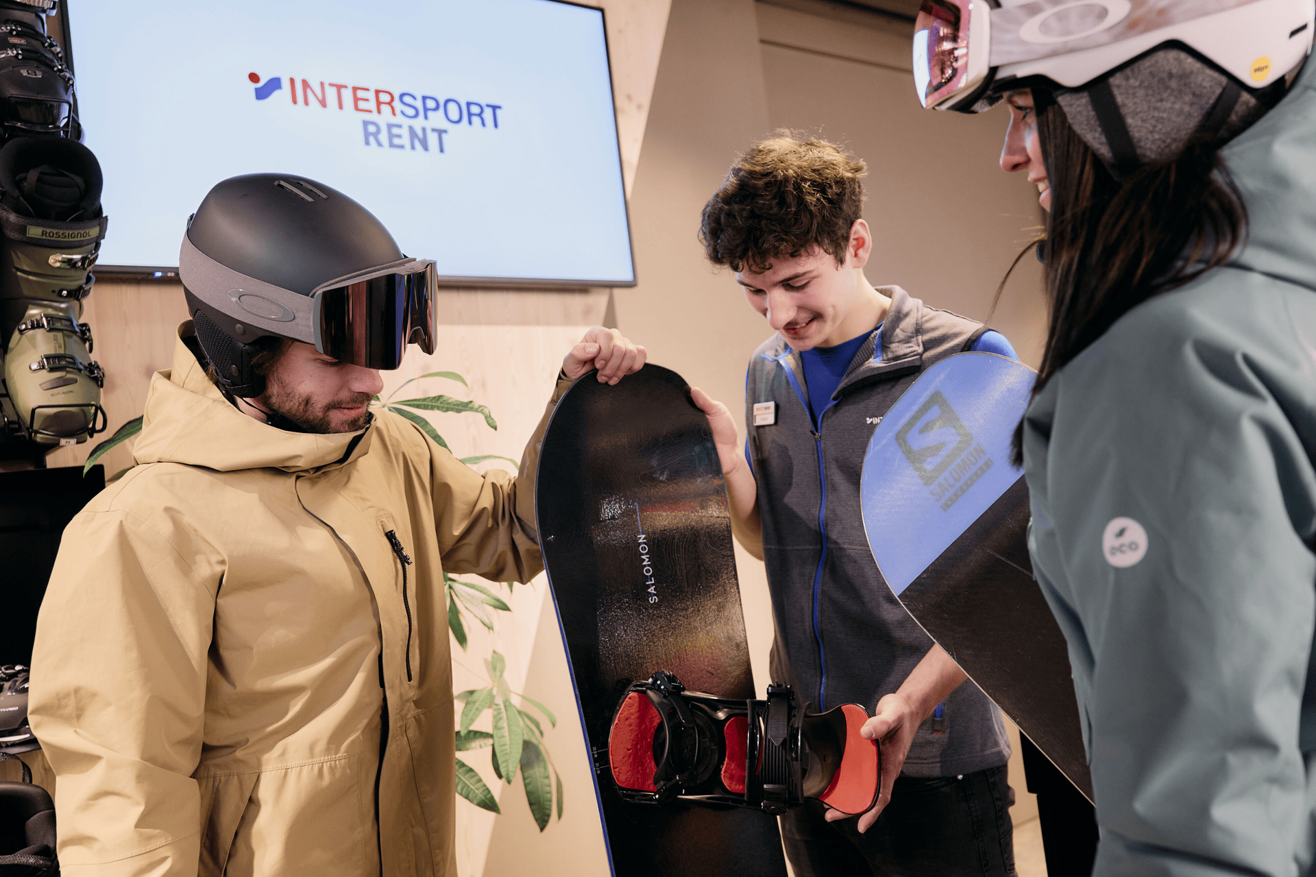 Mitarbeiter zeigt zwei Kunden Snowboards