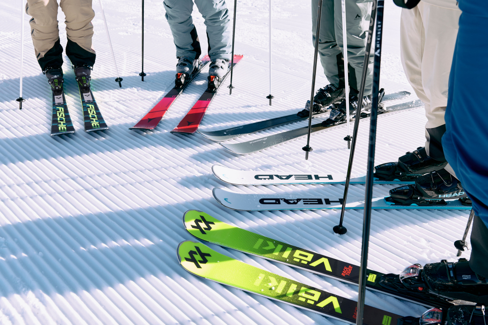 Close-up of 4 pairs of skis in different colors and from different brands.