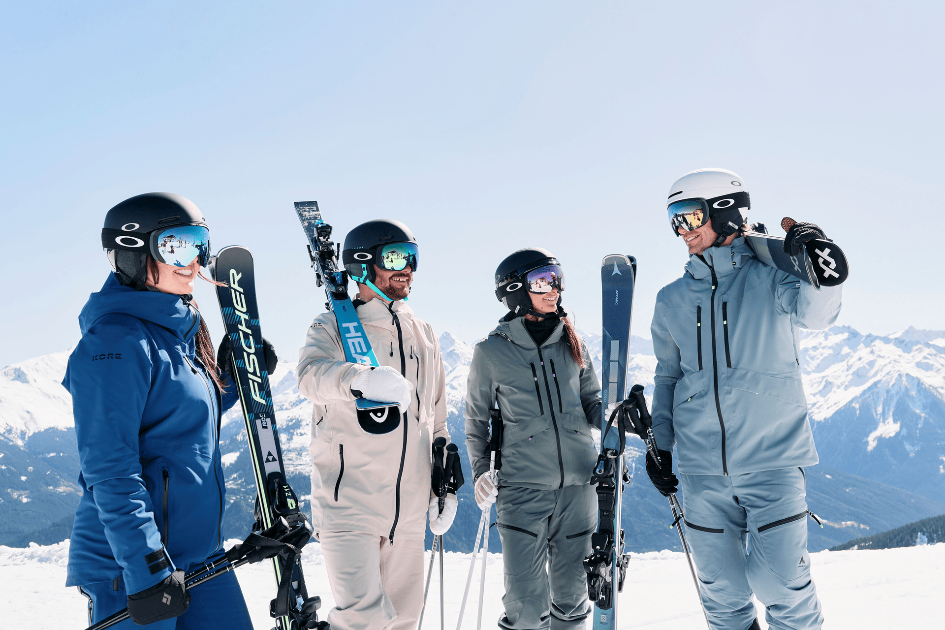 4 Skifahrer stehen im Schnee, lächeln und sehen sich an.